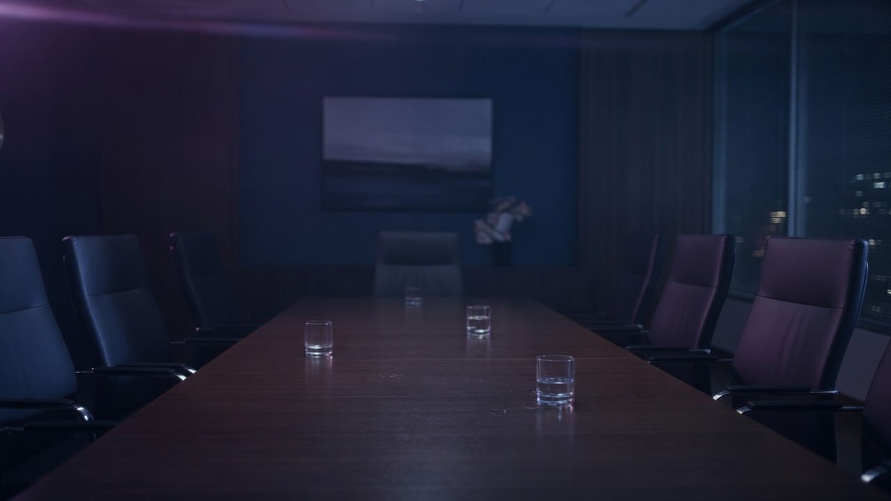 An empty conference table after the meeting, glasses still on the wood.